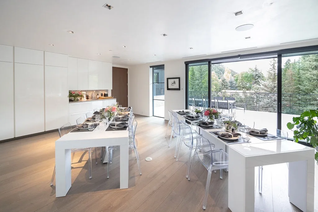A bright dining area with long tables beside large windows opening onto a terrace.