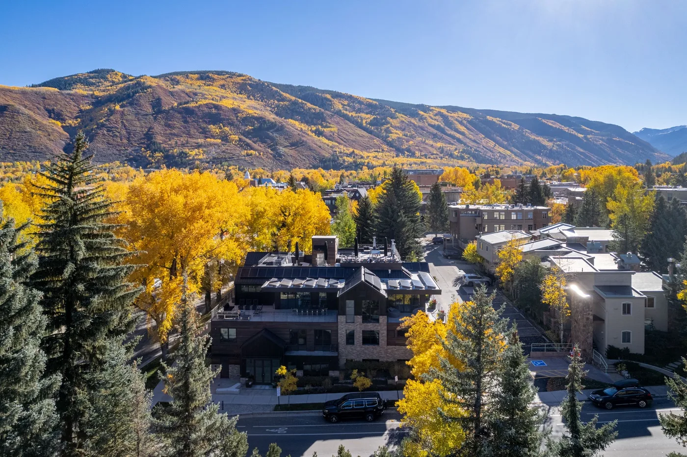 A town sits among bright autumn trees beneath a mountain ridge.