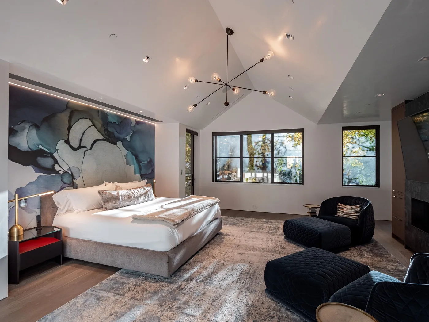 A spacious bedroom features a large bed, abstract wall art, and broad windows.