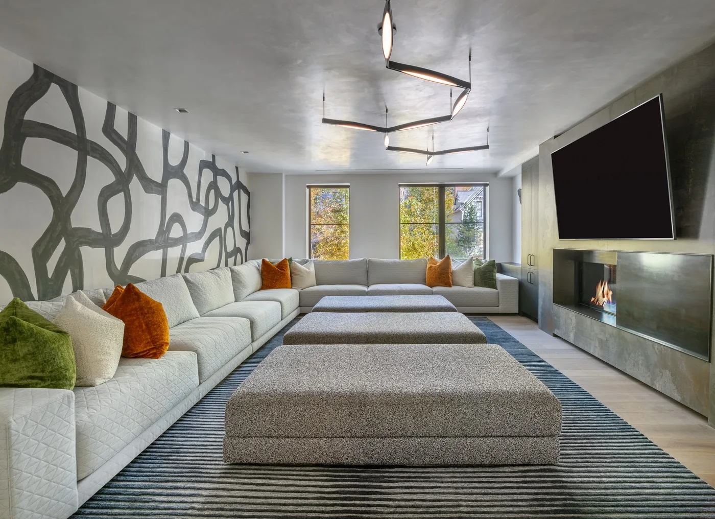 A modern living room with a large sectional sofa, ottomans, and a wall-mounted television.