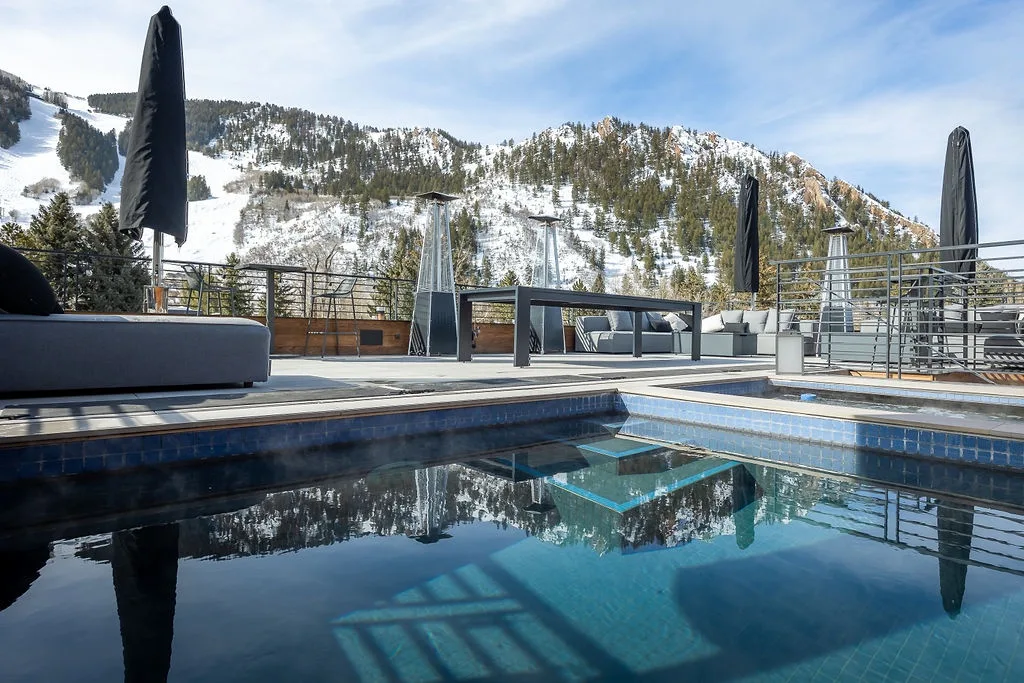 An outdoor pool and terrace overlook a snow-covered mountain.