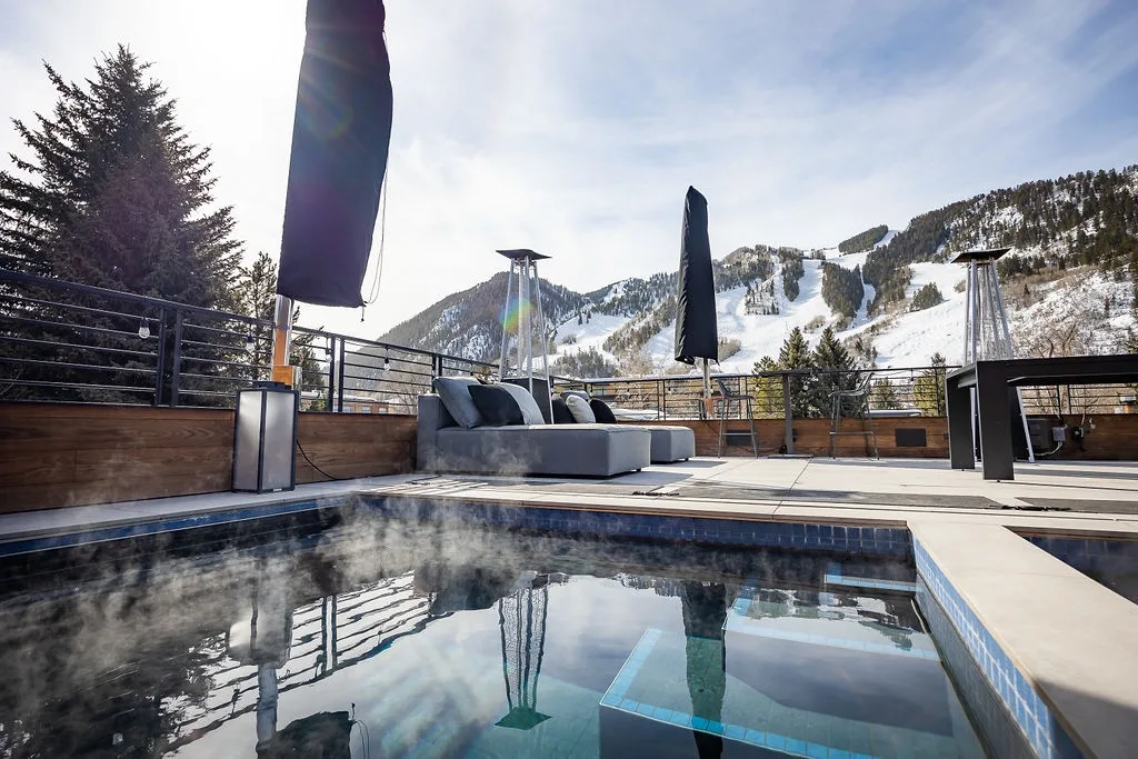 An outdoor pool overlooks a mountain landscape, with lounge seating on the surrounding deck.