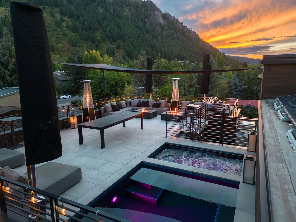 A rooftop terrace with lounge seating, outdoor heaters, and a mountain sunset view.