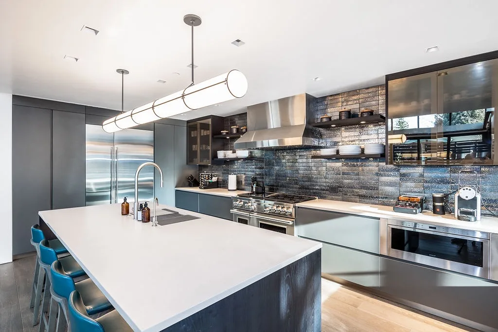A modern kitchen with a large island, blue seating, and stainless steel appliances.