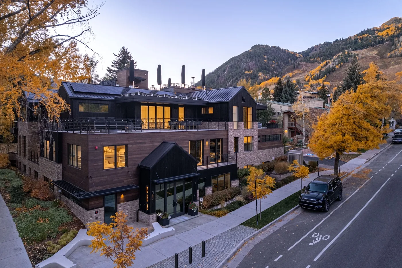 A modern building stands beside a road, with autumn trees and wooded hills behind it.