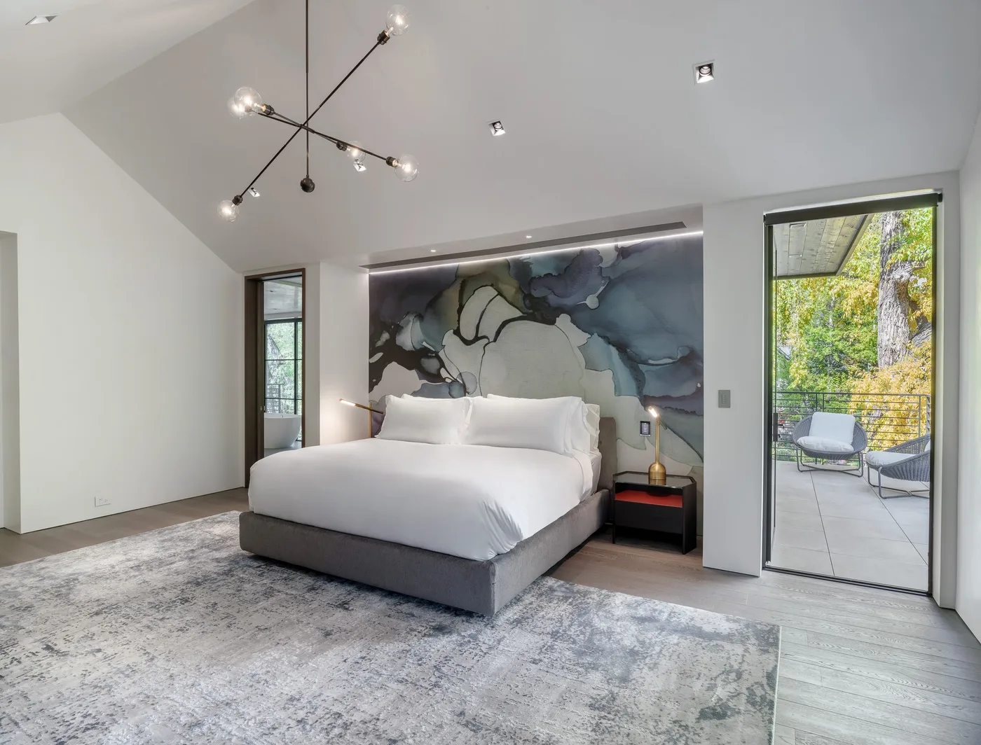 A modern bedroom with a large bed, abstract wall art, and a glass door to a patio.