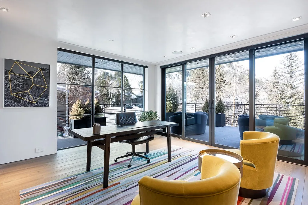 A bright living area with large windows, colorful seating, and a dining table.