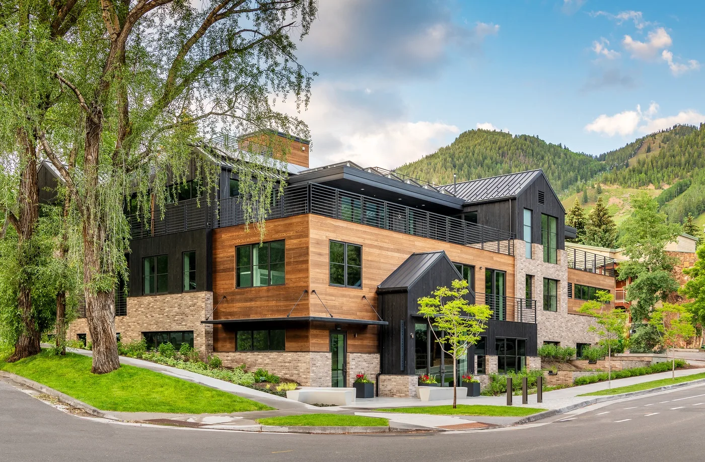 A modern multi-story building stands beside a road, with wooded hills in the background.