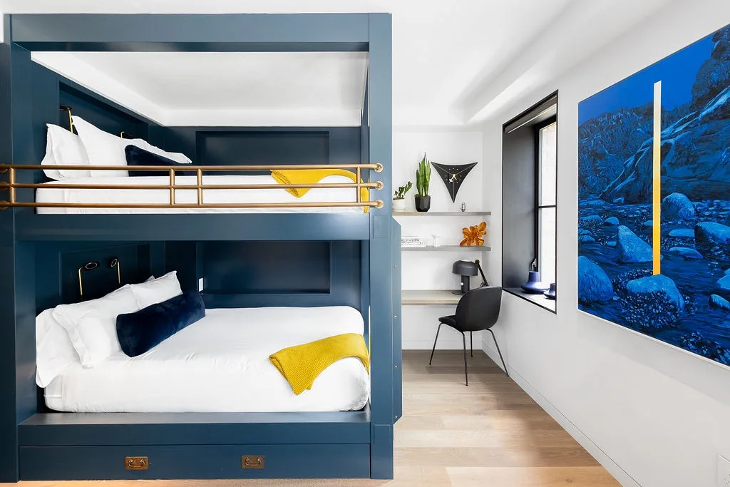 A modern bedroom features a blue bunk bed with white bedding and wall art.