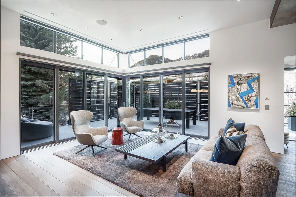 A bright living room with large windows, seating, and a low coffee table.
