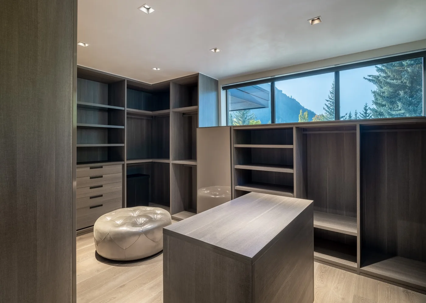 A walk-in closet with dark shelving, drawers, a central island, and a large window.