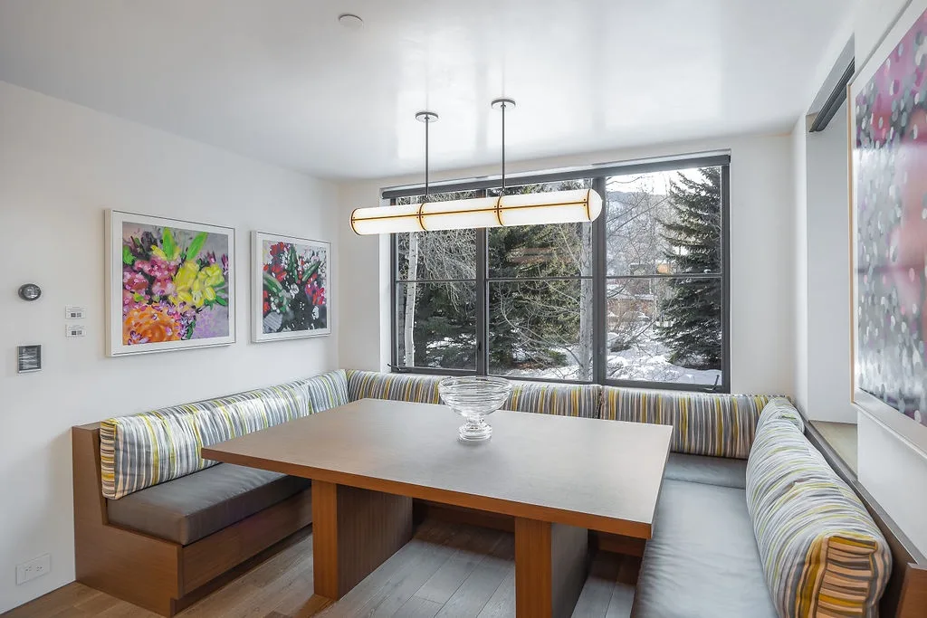 A bright dining nook with a large table, built-in seating, and wide windows.