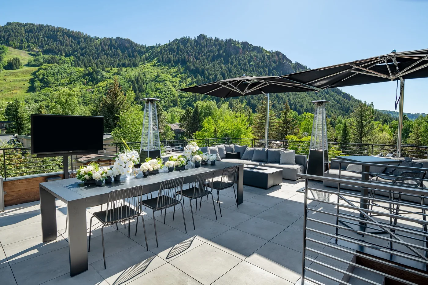 An outdoor terrace with dining and lounge seating beneath a canopy, overlooking green hills.