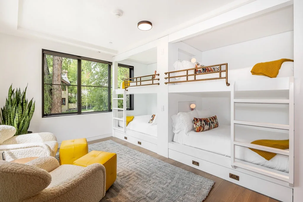 A bright bedroom features built-in bunk beds, a large window, and a seating area.