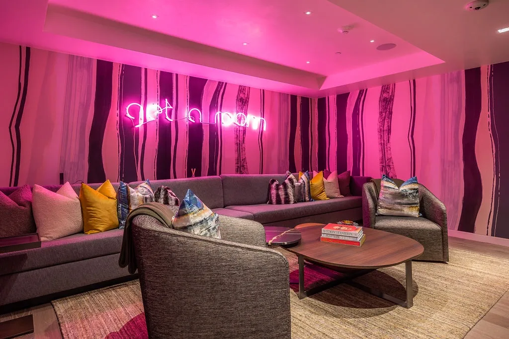 A lounge seating area with cushioned seating and a low coffee table under pink lighting.