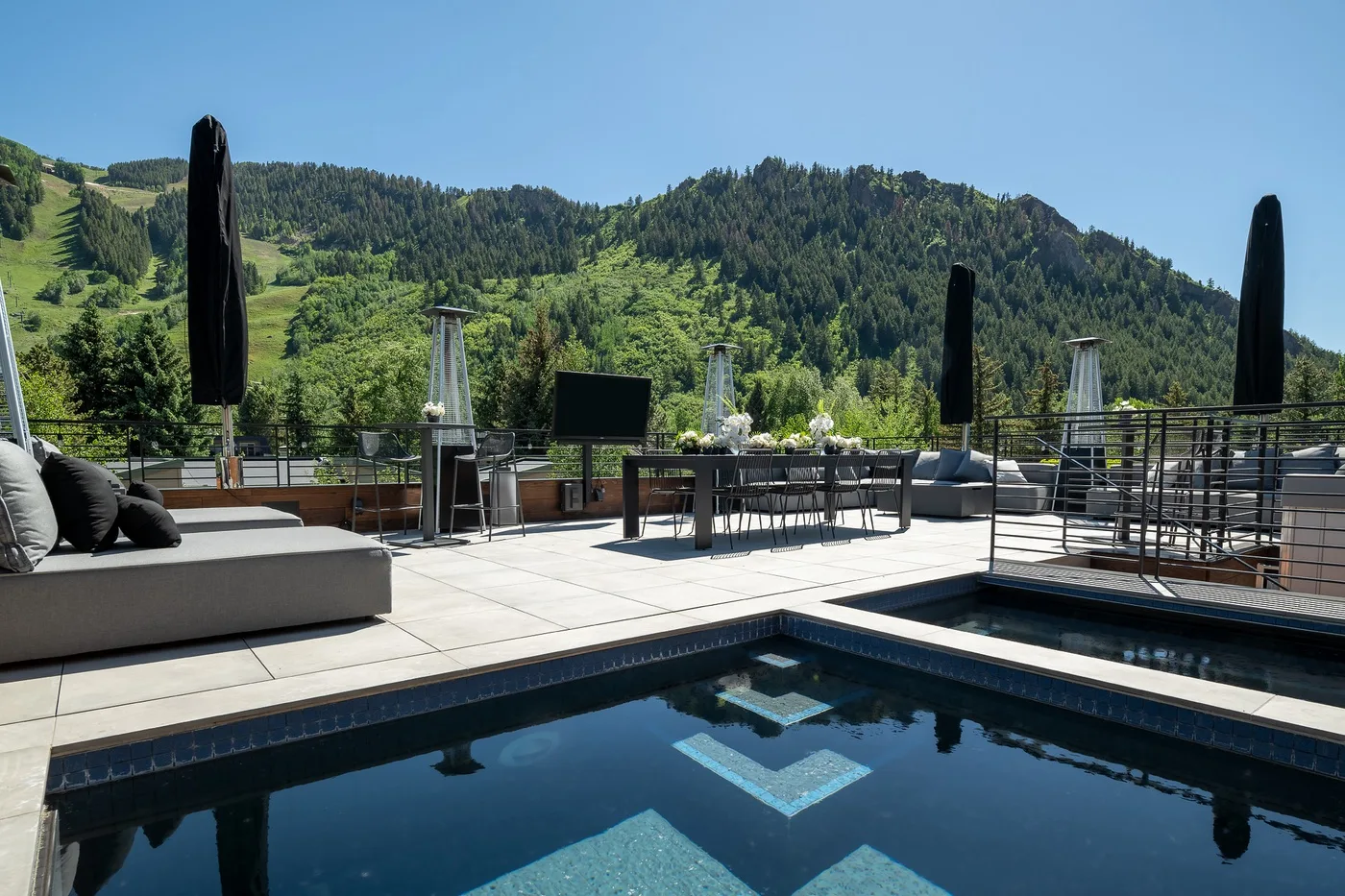 An outdoor terrace overlooks a pool, with seating and wooded hills beyond.