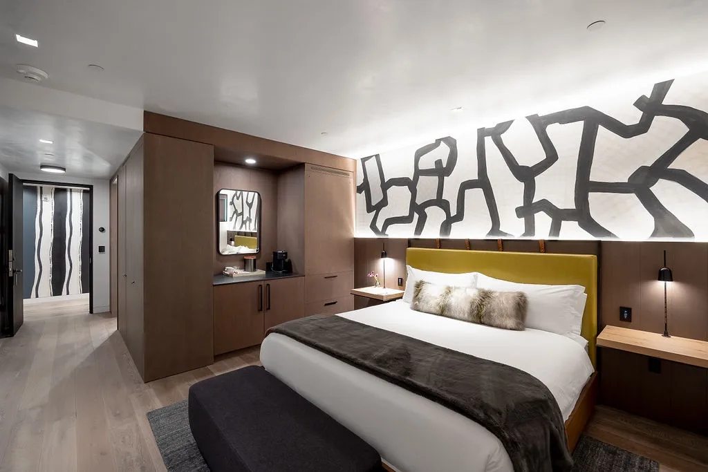 A modern bedroom with a bed, dark headboard, and bold wall artwork.