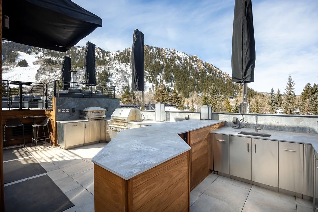 An outdoor kitchen with a central counter, stainless steel cabinets, and a mountain view.