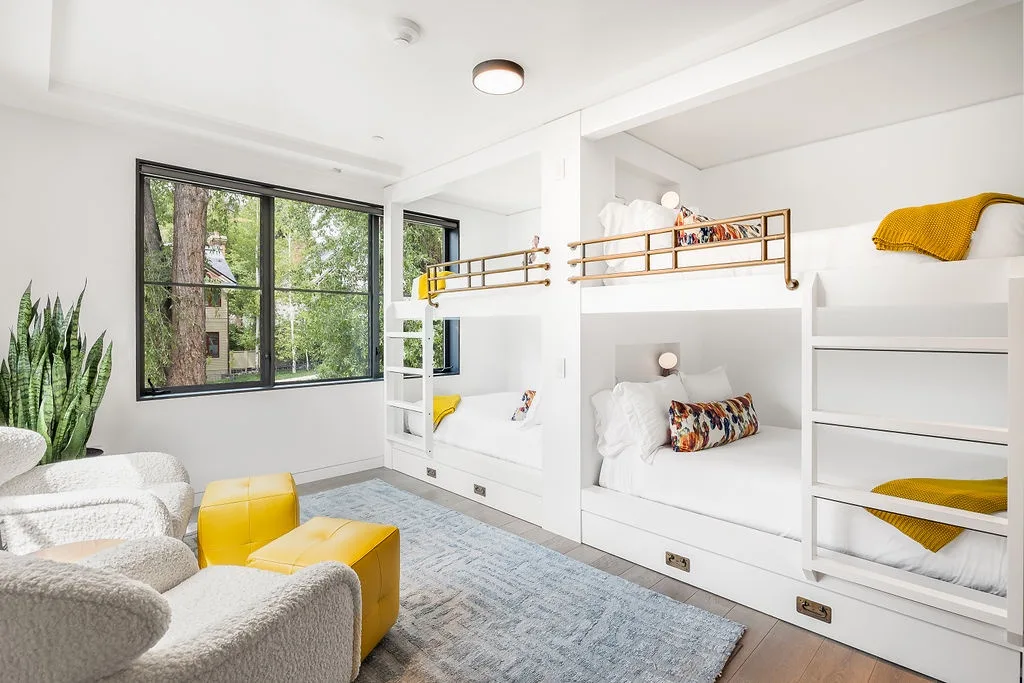 A bright bedroom with built-in bunk beds, large windows, and a seating area.