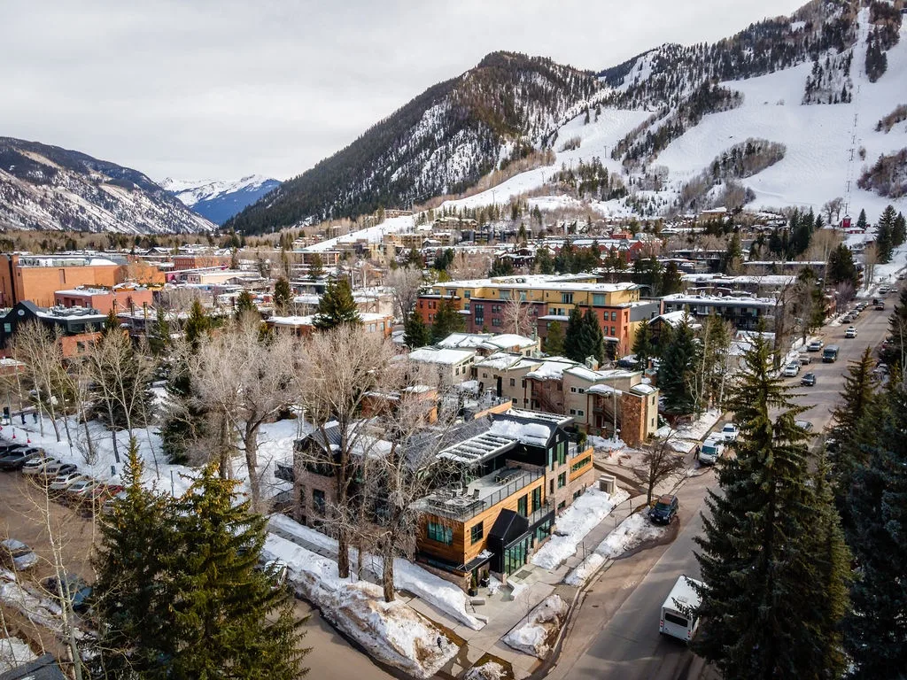 A snowy mountain town with buildings and roads beneath wooded slopes.