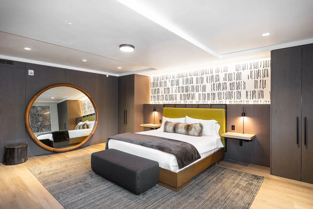 A bedroom with a large bed, a round wall mirror, and dark built-in cabinets.