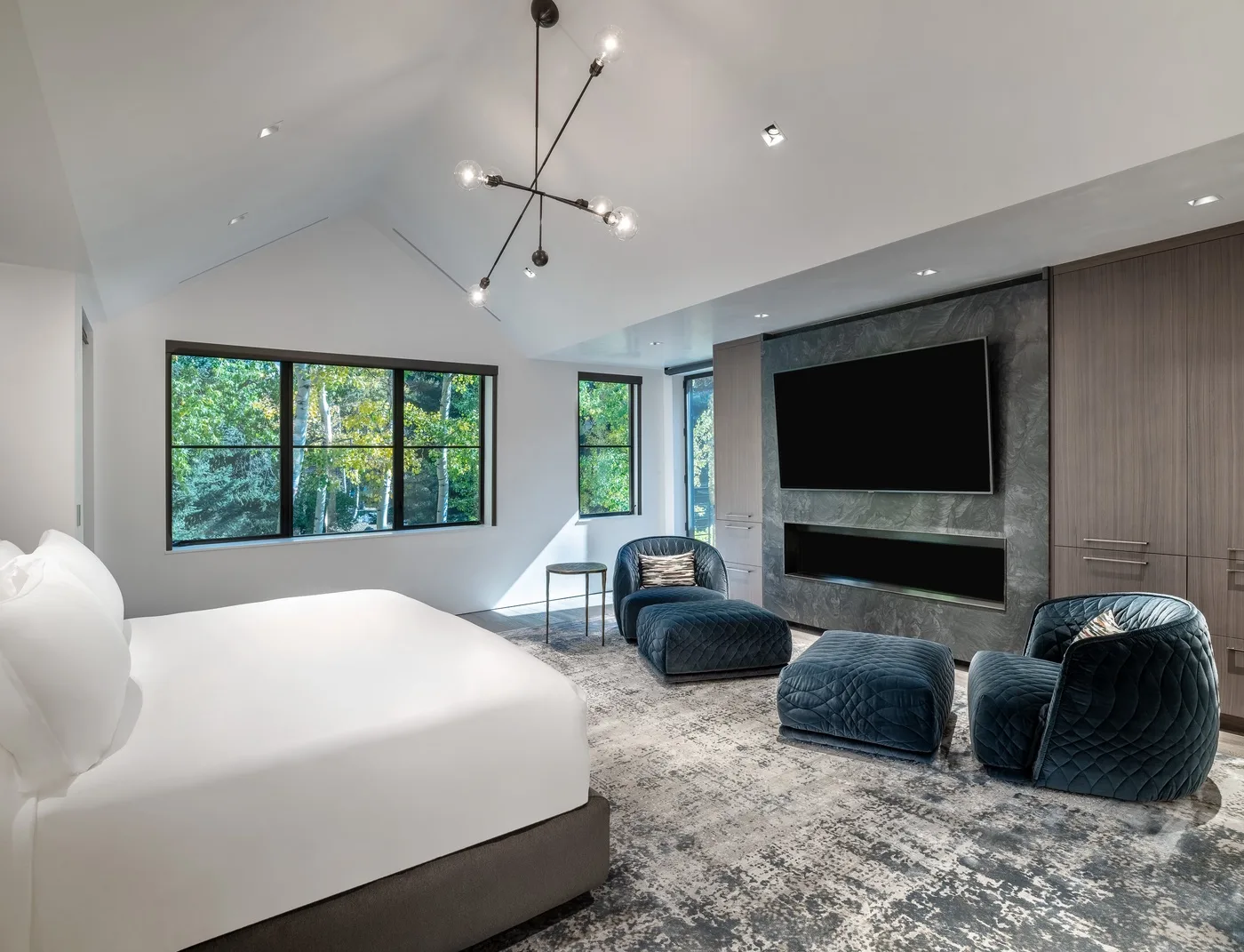 A modern bedroom with a bed, lounge seating, and a wall-mounted television.