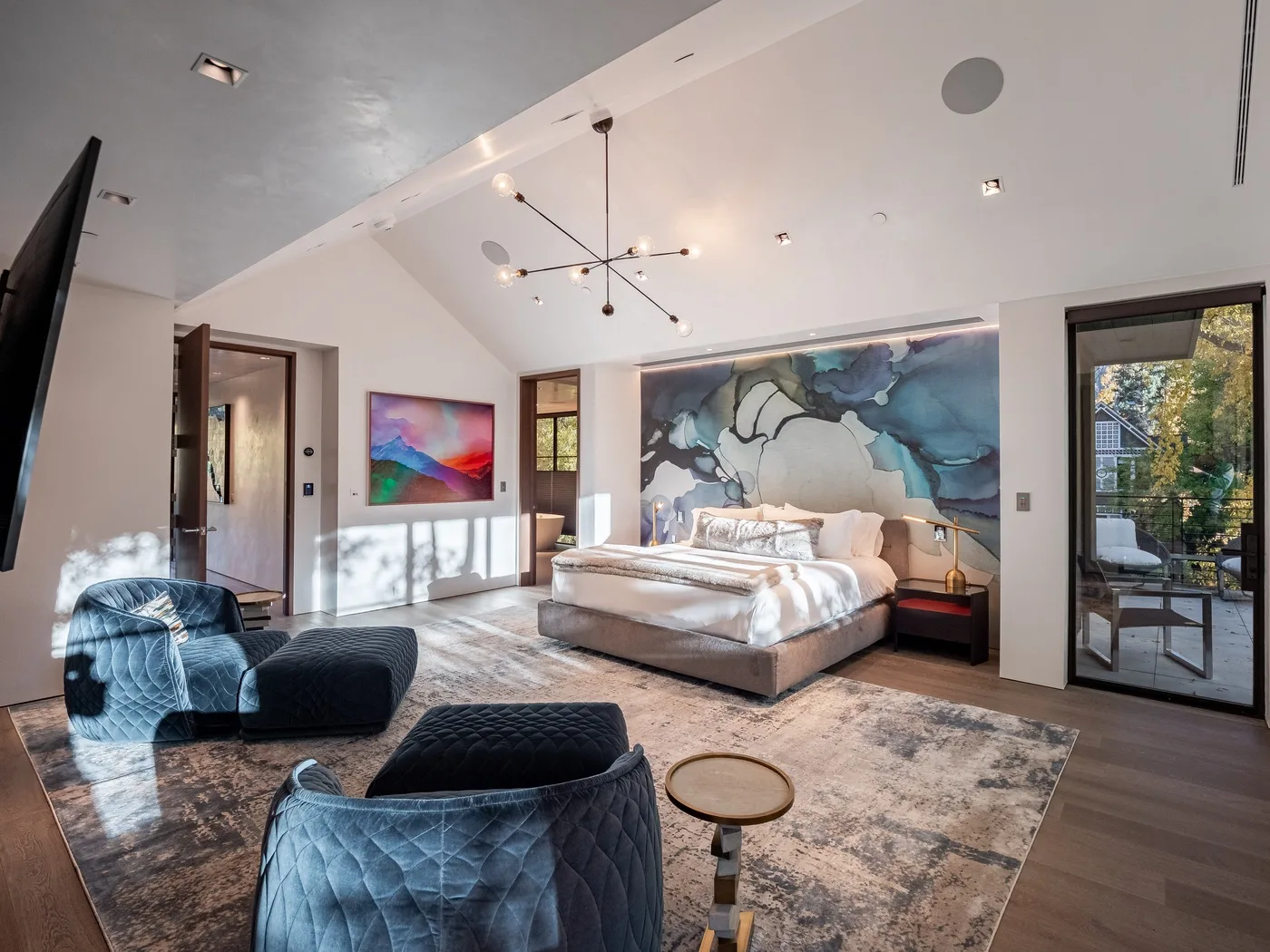 A spacious bedroom with a bed, lounge seating, and a large mural behind the bed.