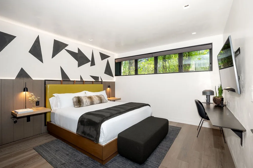 A modern bedroom with a bed, patterned wall, and desk beside a window.