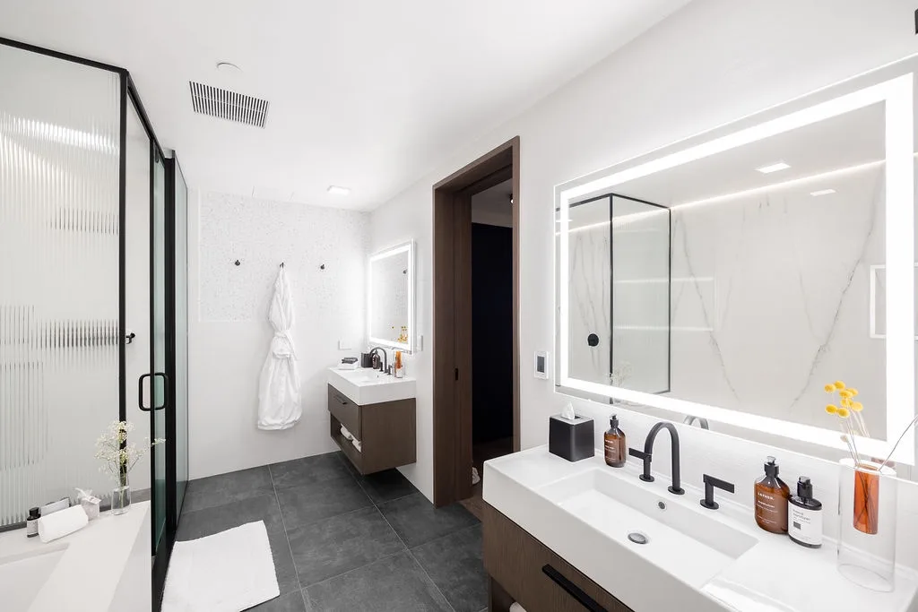 A bright bathroom with a double vanity, large mirror, and glass shower.