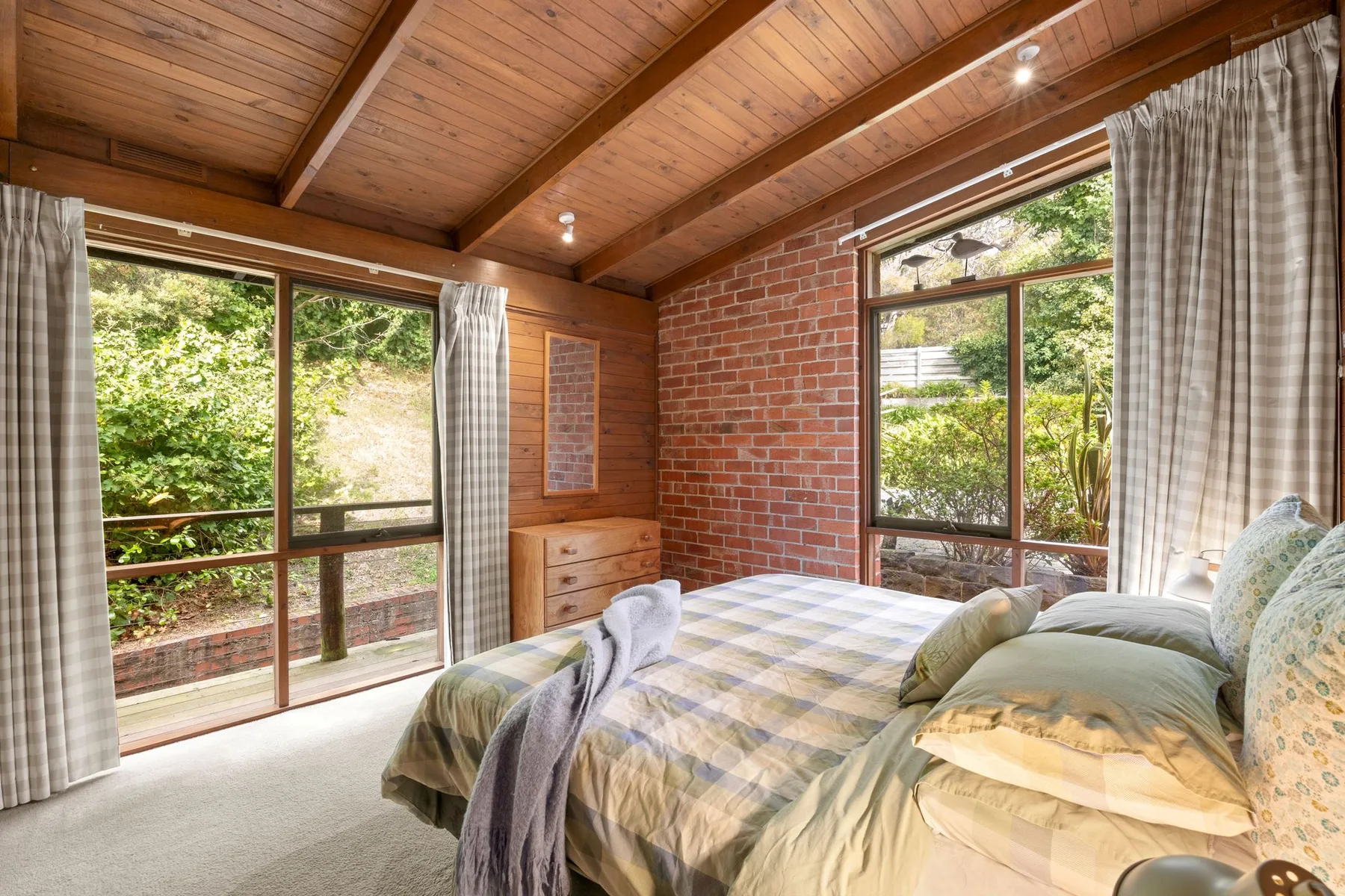 A bedroom with a bed beside large windows overlooking greenery.