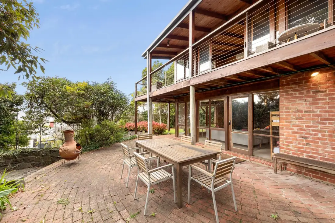A brick-paved outdoor patio with a wooden dining table beside the house.