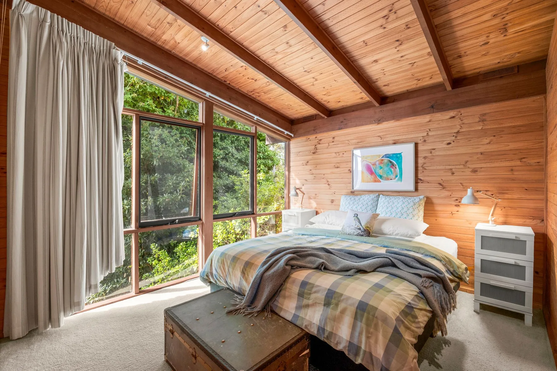 A bedroom with a bed beside large windows overlooking greenery.