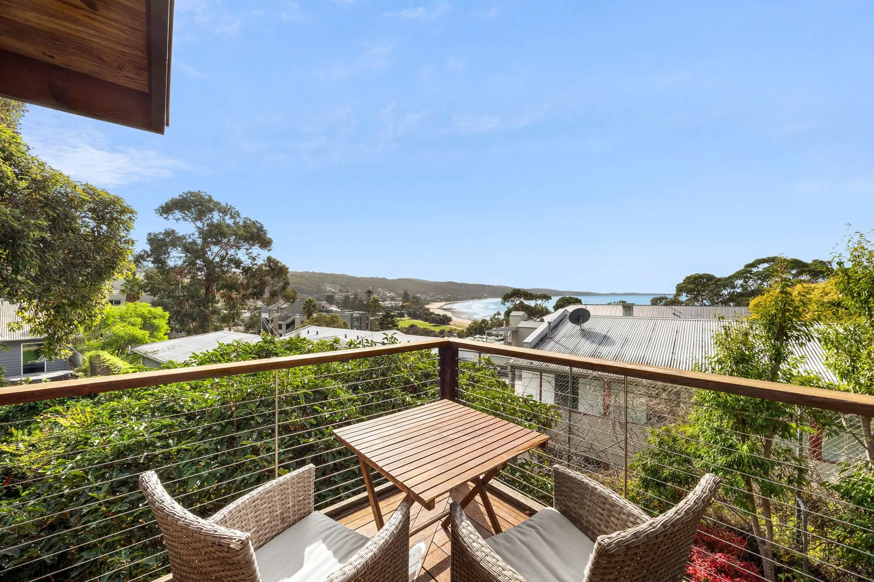 A balcony dining area overlooks rooftops, trees, and the ocean.