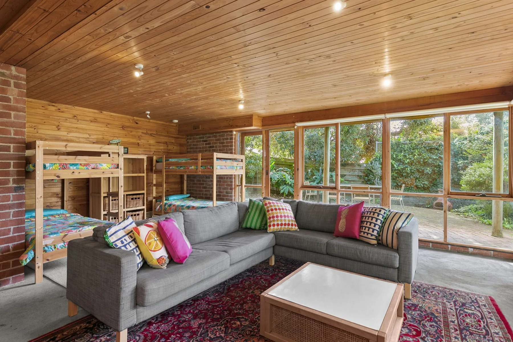 A wood-paneled lounge with bunk beds, sectional seating, and windows facing a garden.