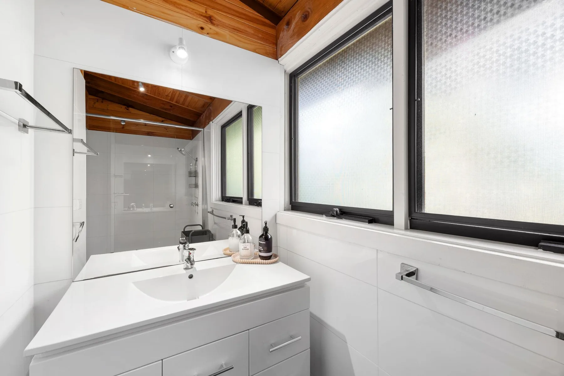 A bright bathroom with a sink vanity and large frosted windows.