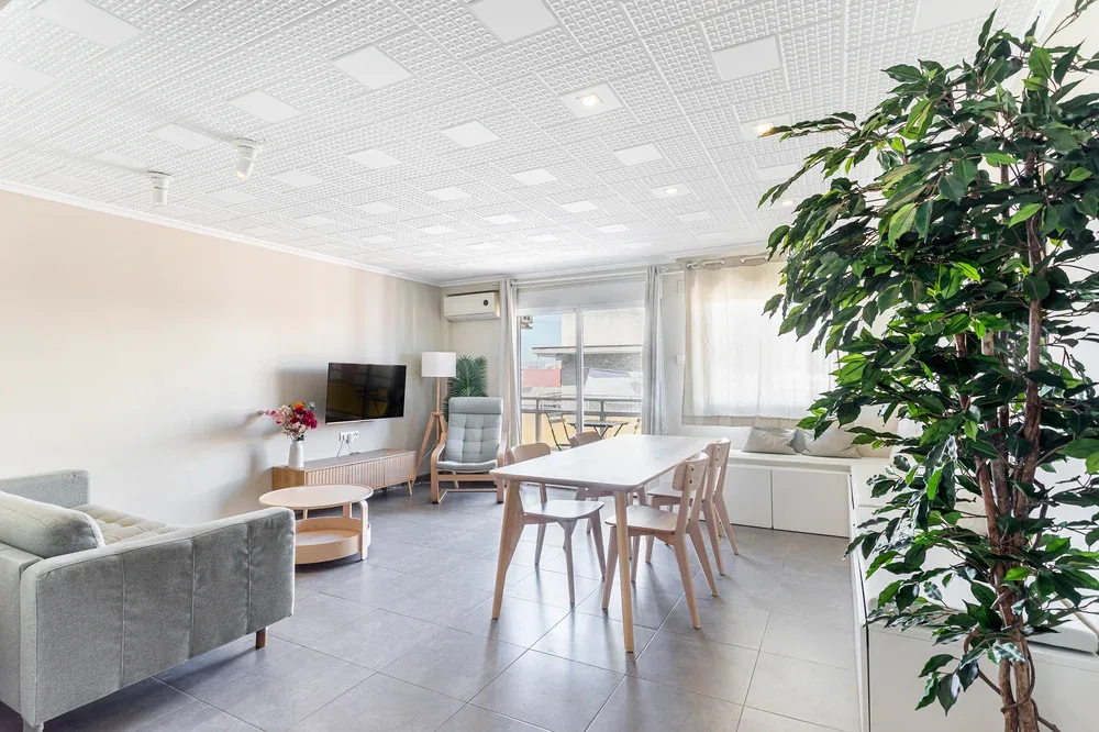 Una luminosa sala de estar y comedor con asientos, una mesa y una gran planta frondosa.