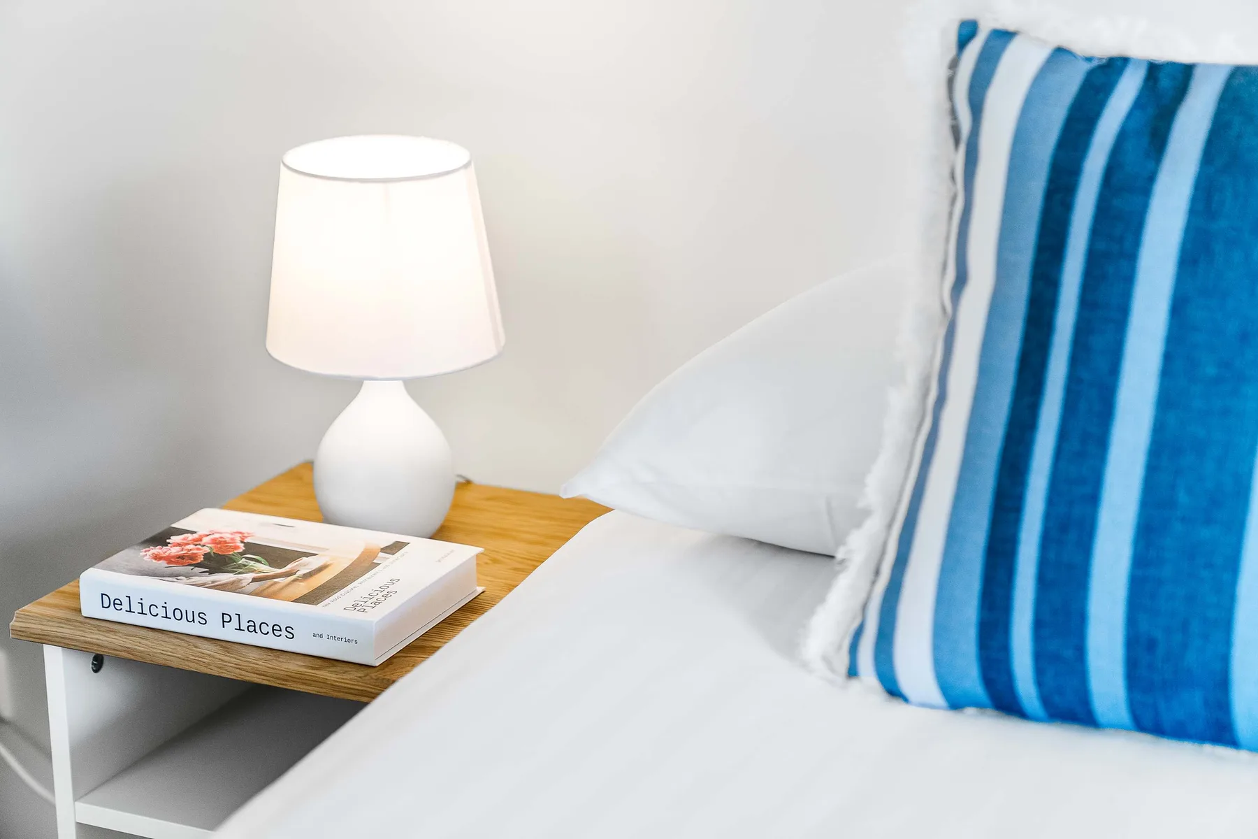 A bedroom bed with a blue striped pillow beside a bedside table and lamp.