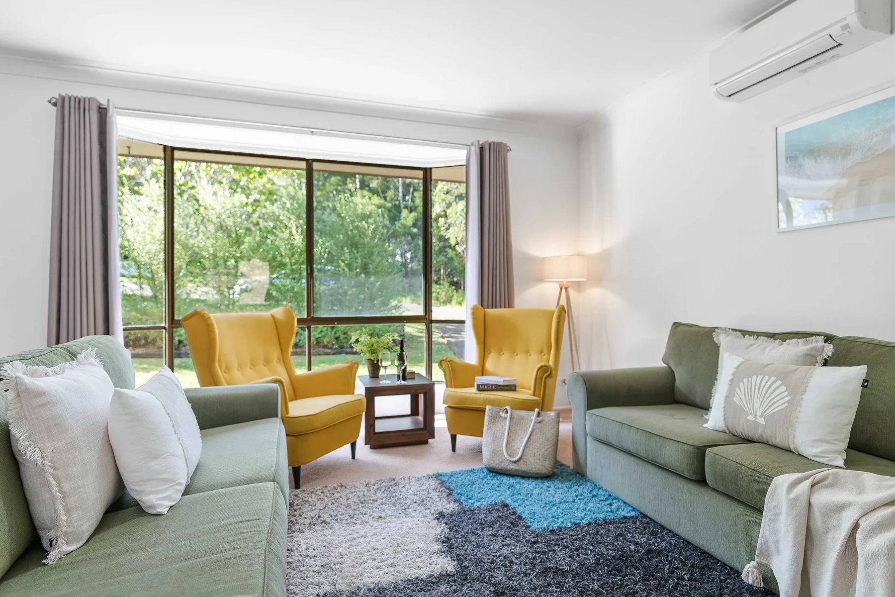 A bright living room with seating beside a large window overlooking greenery.
