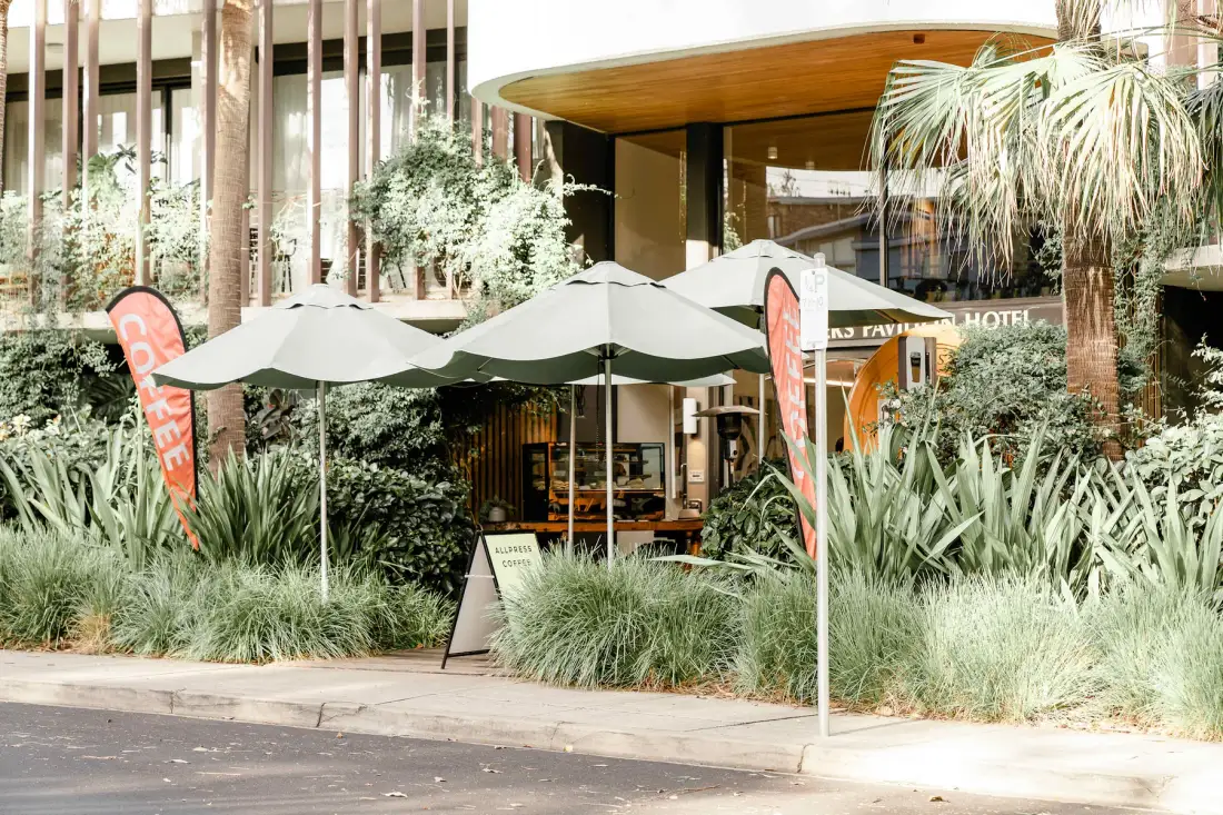 A hotel entrance with outdoor umbrellas and landscaped greenery.