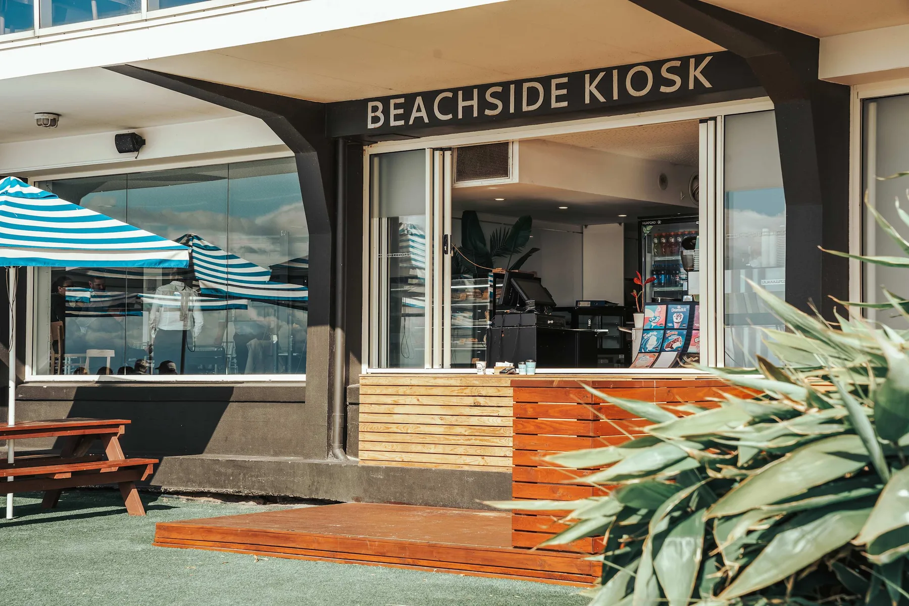 A beachside kiosk storefront with outdoor seating and striped awnings.