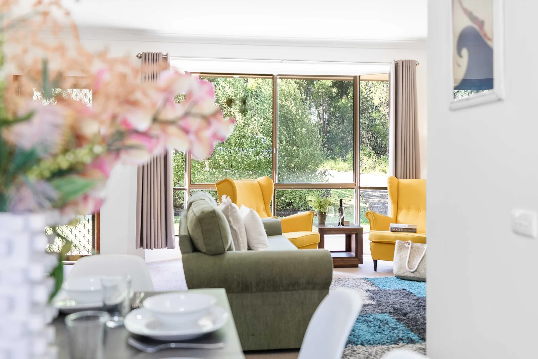 A bright living room with seating, yellow armchairs, and large windows overlooking greenery.