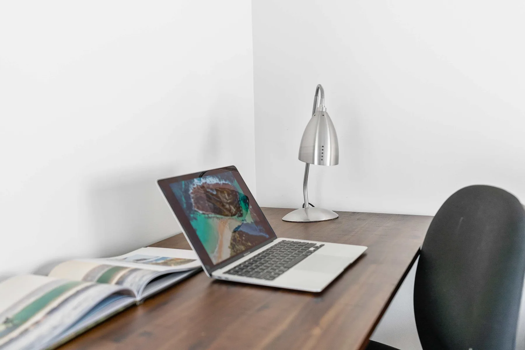 A desk workspace with an open laptop, reading material, and a desk lamp.
