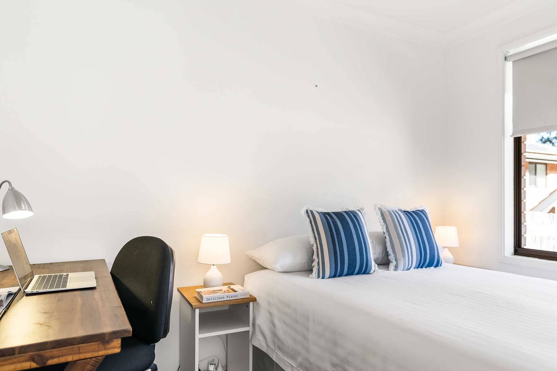 A bright bedroom with a neatly made bed and a small desk beside it.