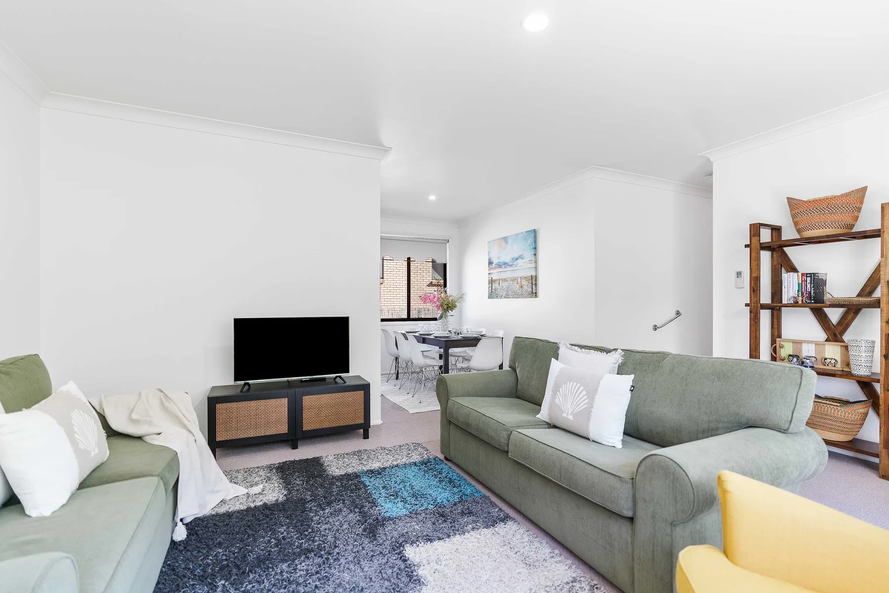 A bright living room with pale seating, a television, and a colorful rug.