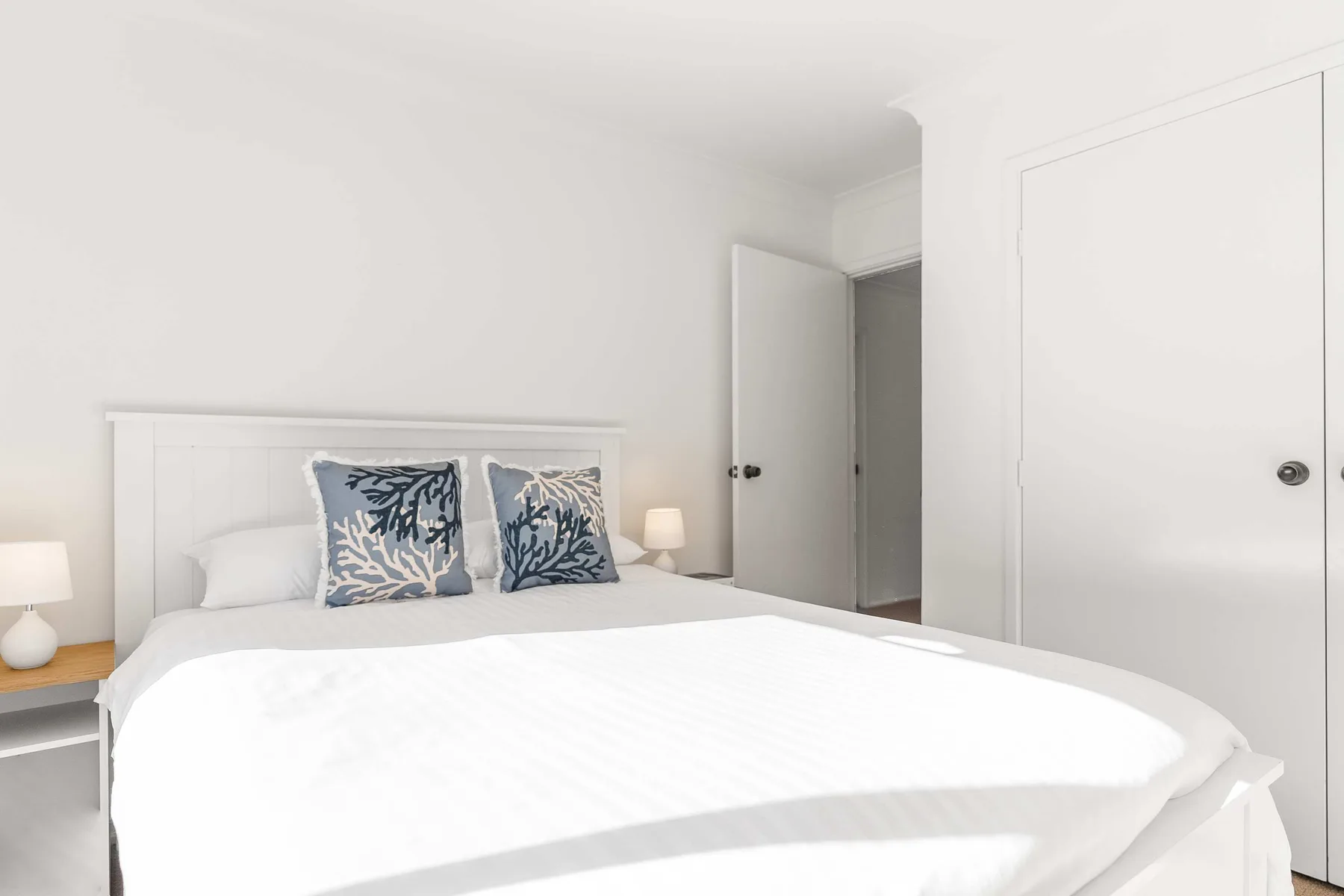 A bright bedroom with a white bed and patterned pillows.