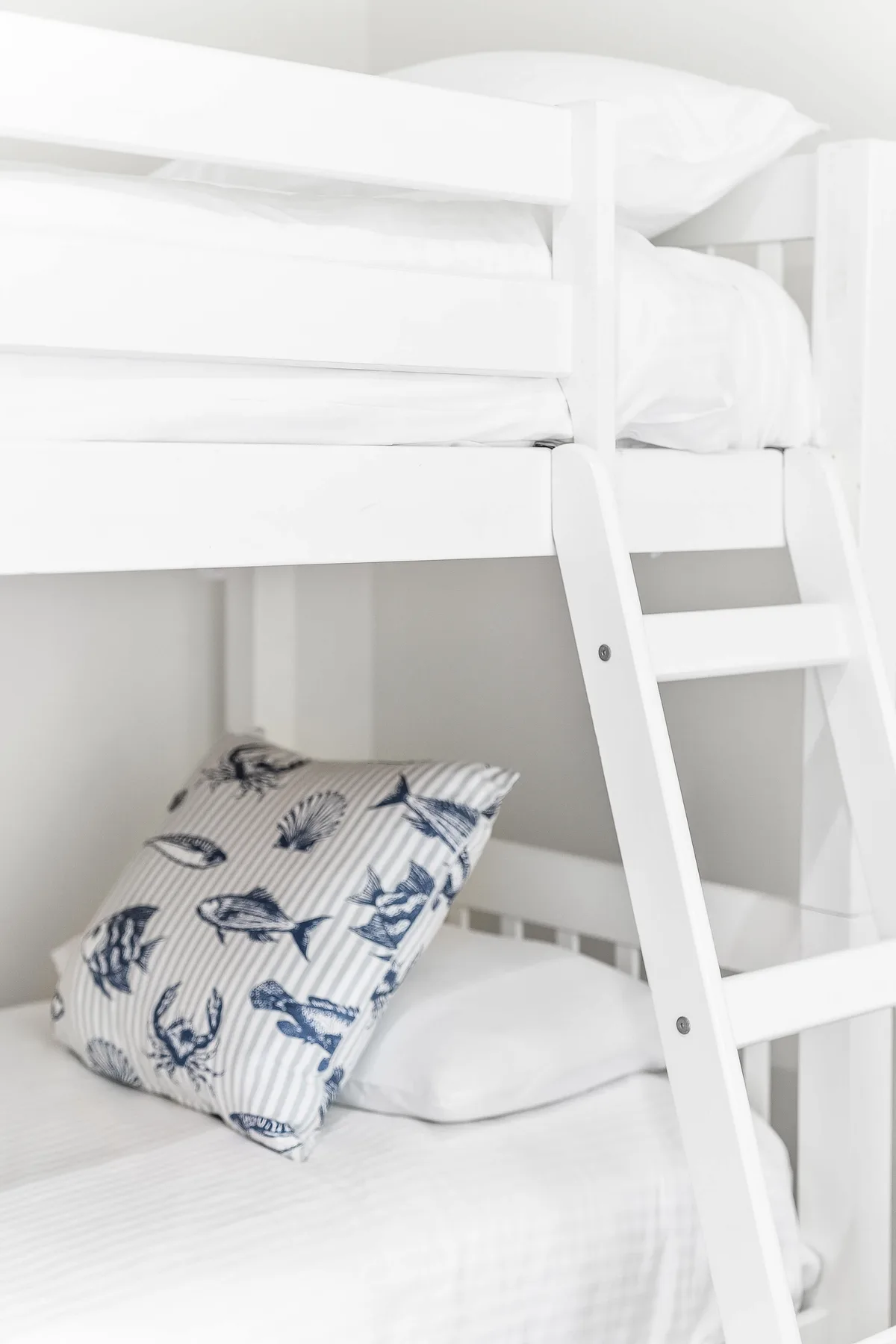 A bright bedroom with white bunk beds and patterned pillows.