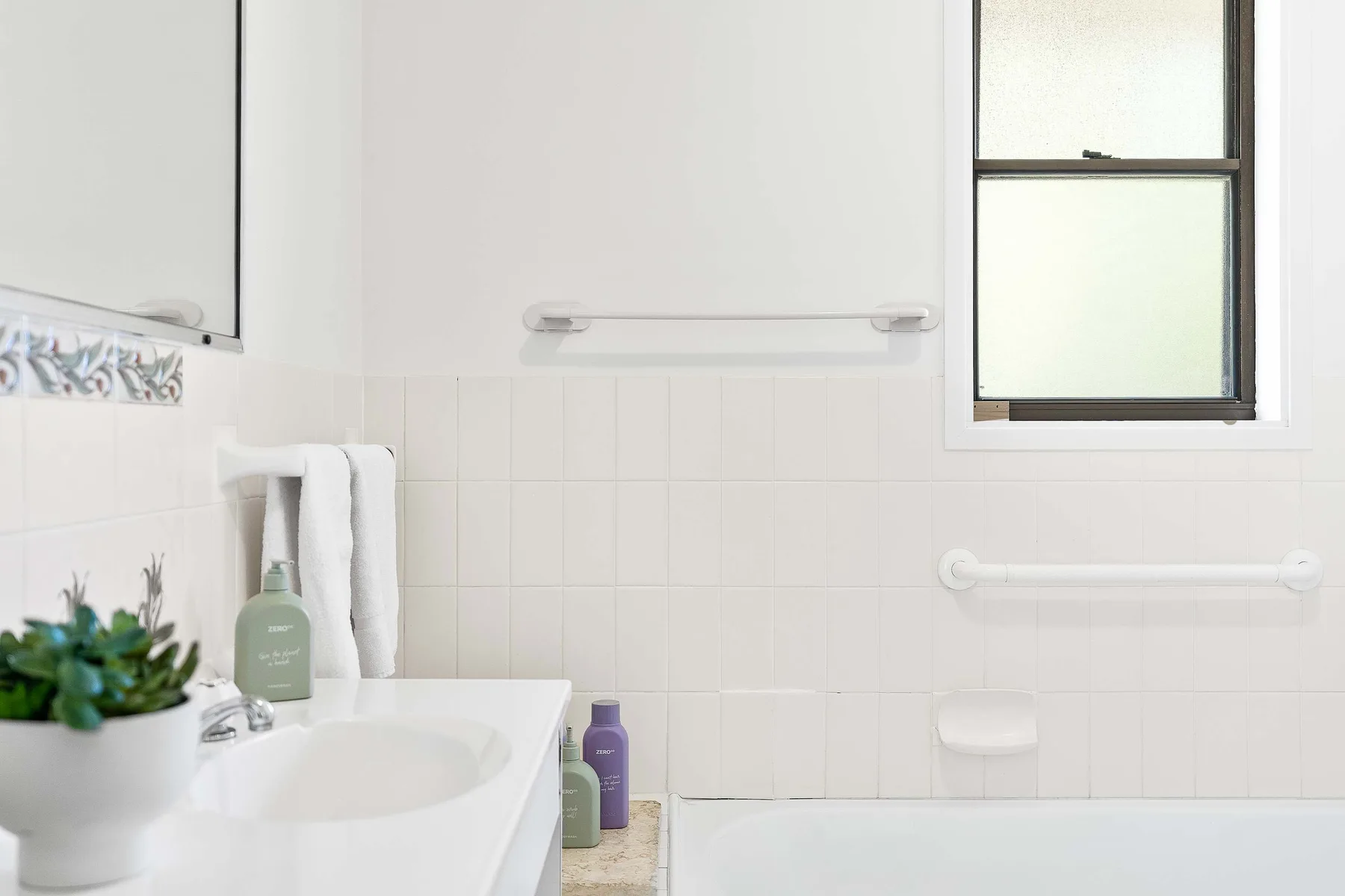 A bright bathroom with a sink, tiled walls, and a window.