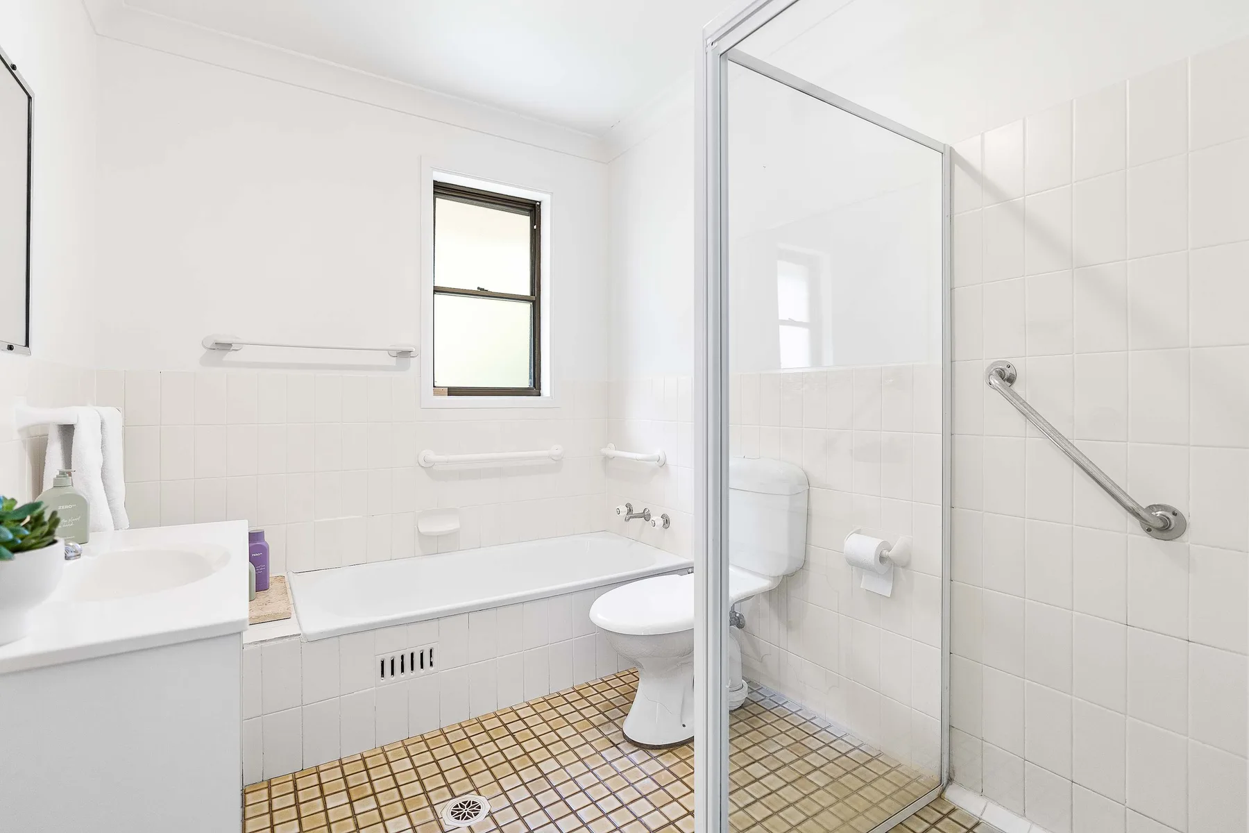 A bright tiled bathroom with a bathtub, sink, and shower.