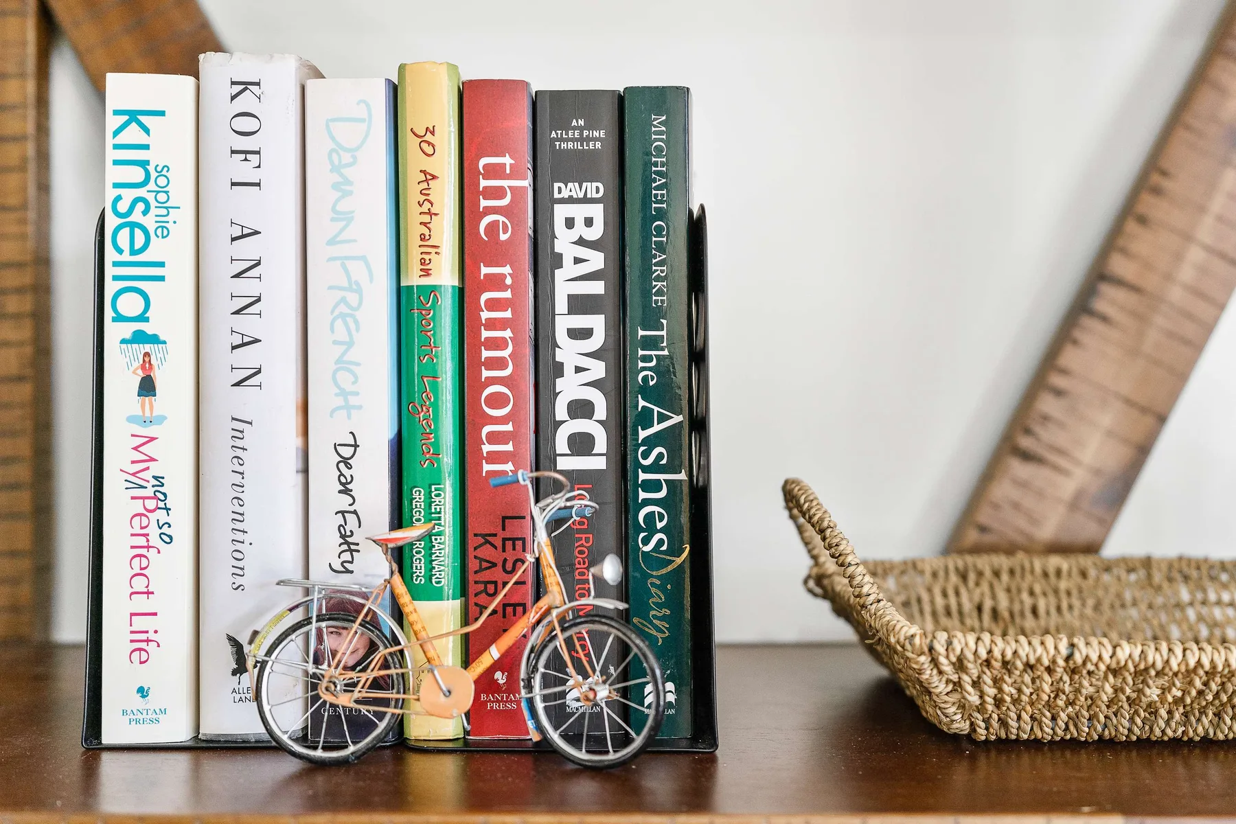 A row of books and a small bicycle ornament sit on a wooden shelf.