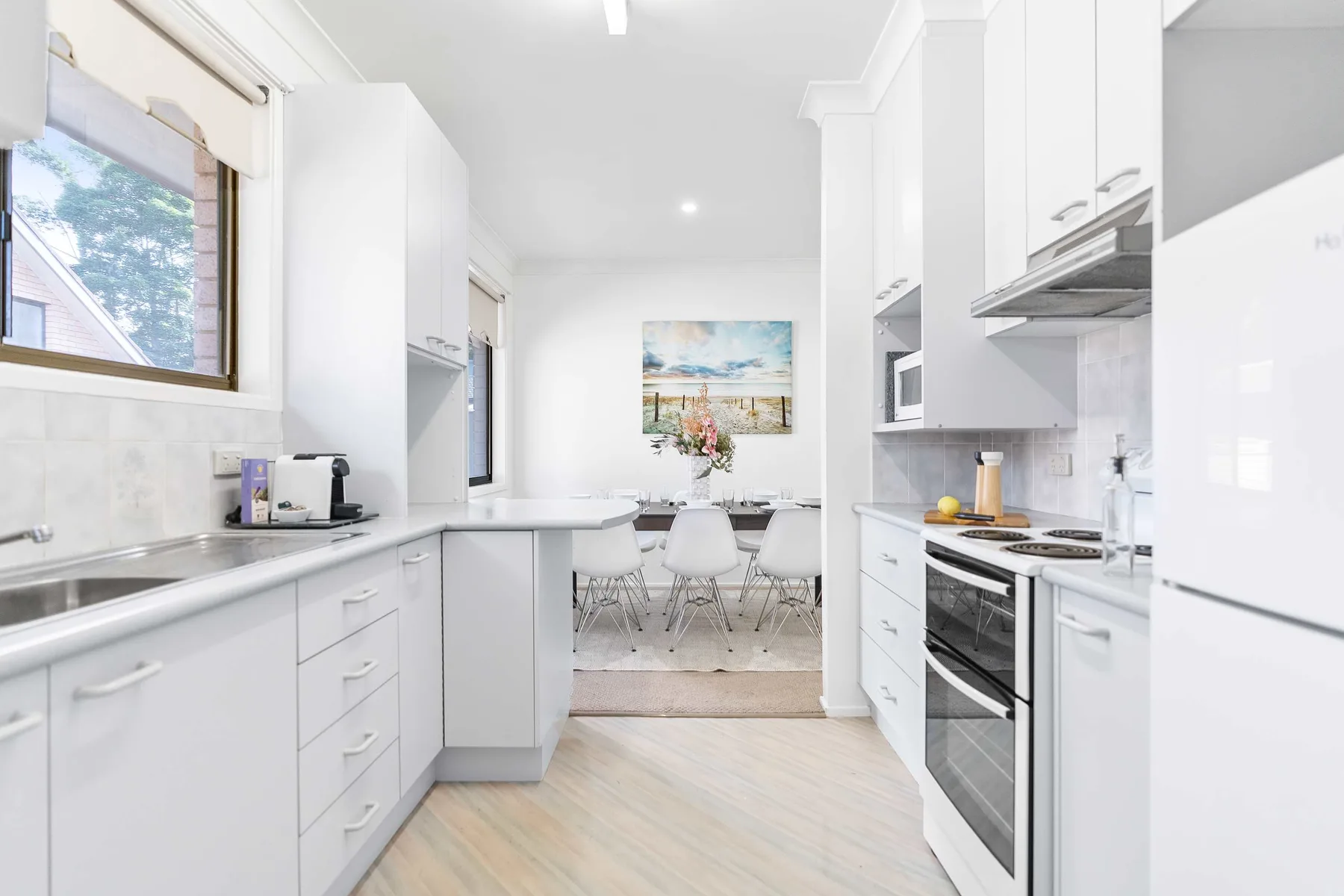 A bright white kitchen opens onto a dining area with a table and chairs.